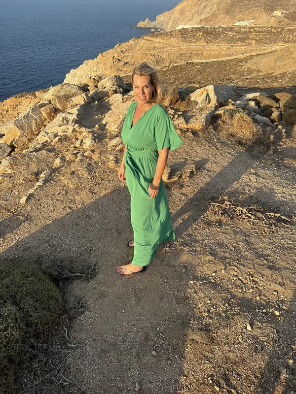 Angélique in een groene jurk op de rotsen boven zee op Kreta